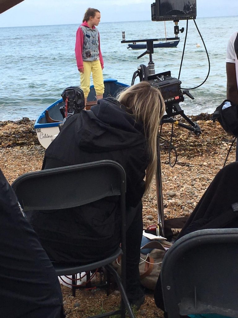 A film crew on the beach, filming King's InterHigh pupil and actress, Bella Ramsey, who is stood in a boat.