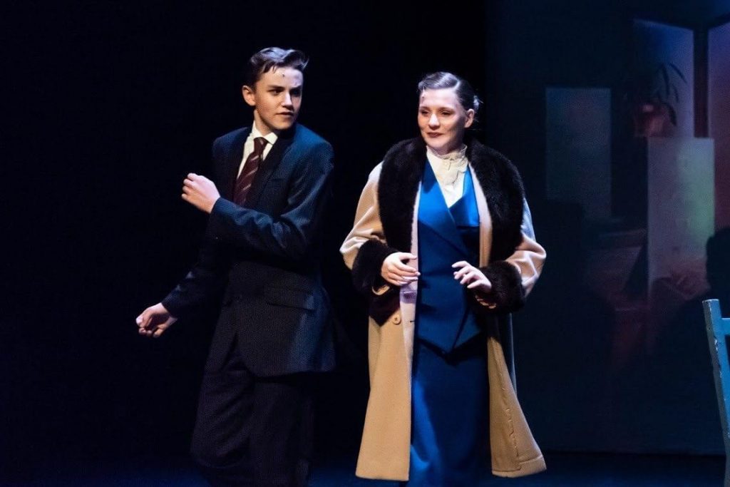 King's InterHigh pupil & musical actor, Daniel Wilmott, on stage wearing a suit next to an actress wearing a blue blazer and fur-lined coat.