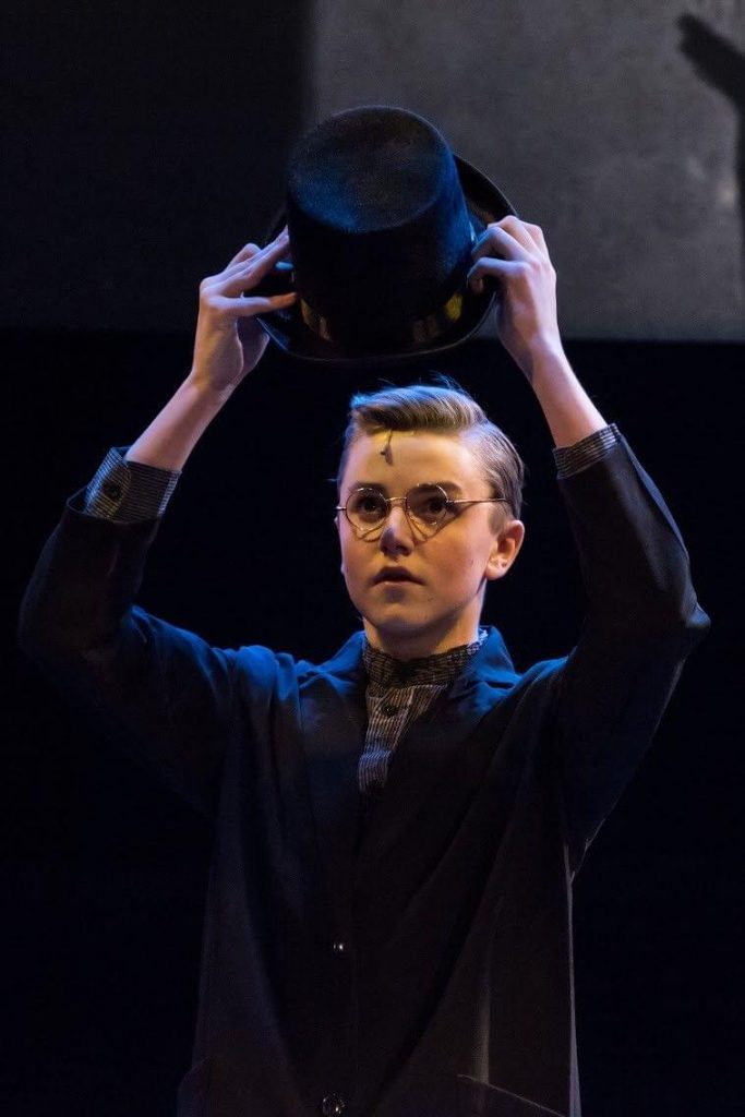 King's InterHigh pupil & musical actor, Daniel Wilmott, performing on stage and holding at hat in above his head.