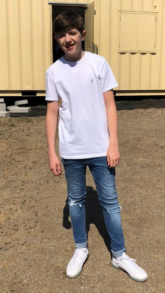 King's InterHigh pupil & actor, Gene, standing in front of a cream coloured container. He's smiling & wearing a white t-shirt.