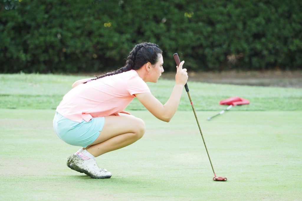 King's InterHigh pupil & golfer, Darcy Harry, crouching on a putting green with a putter in hand wearing pastel coloured golf attire.